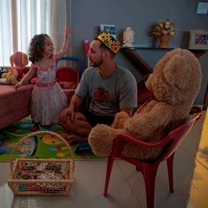 Young girl in a princess dress with a man wearing a crown with a Teddy bear in the foreground